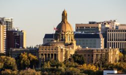 Alberta Legislature Building's domed sandstone facade in Edmonton, lit by evening sun above autumn trees